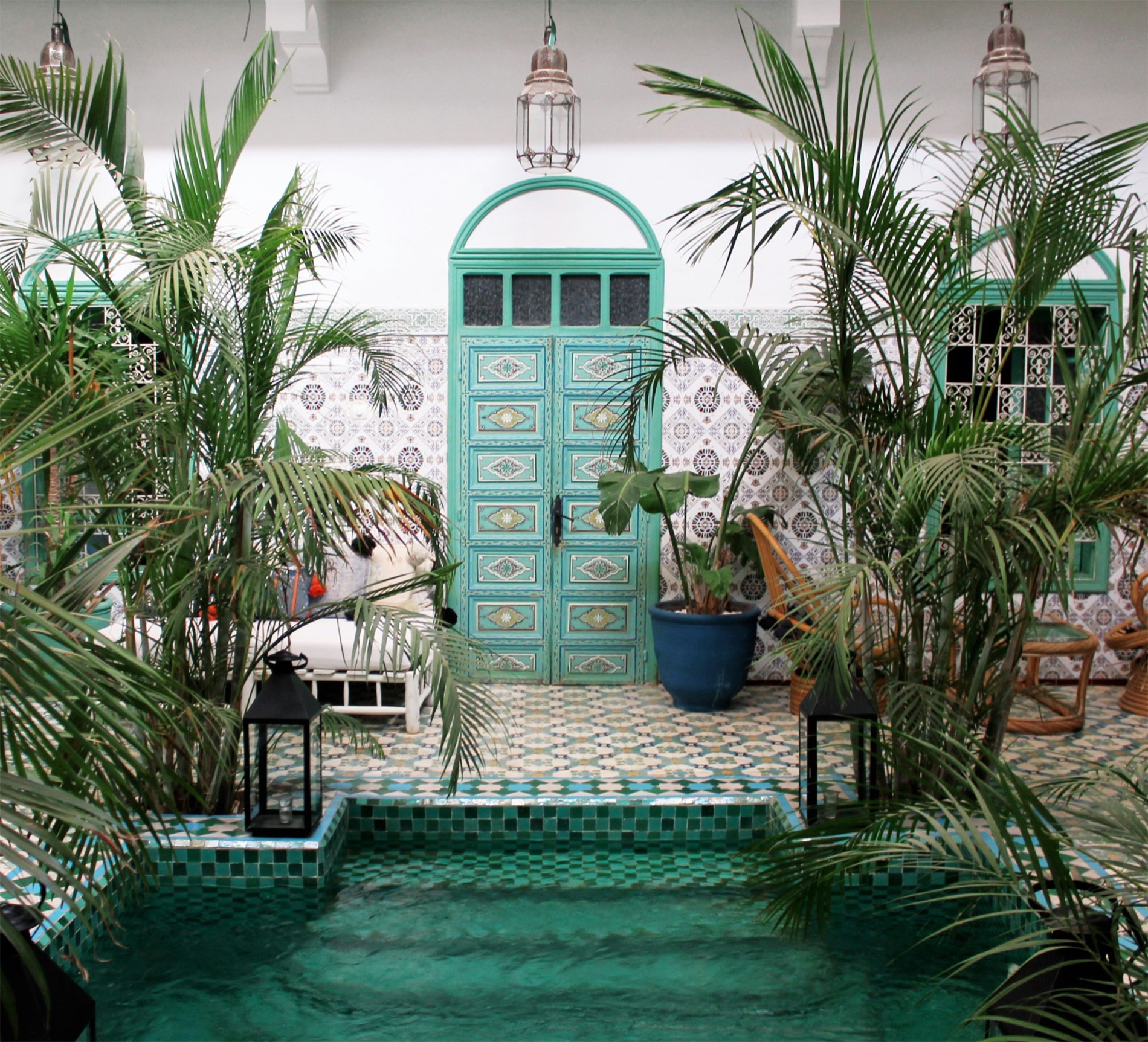 Riad courtyard in Marrakech with a green zellige plunge pool, painted arch door, and palms