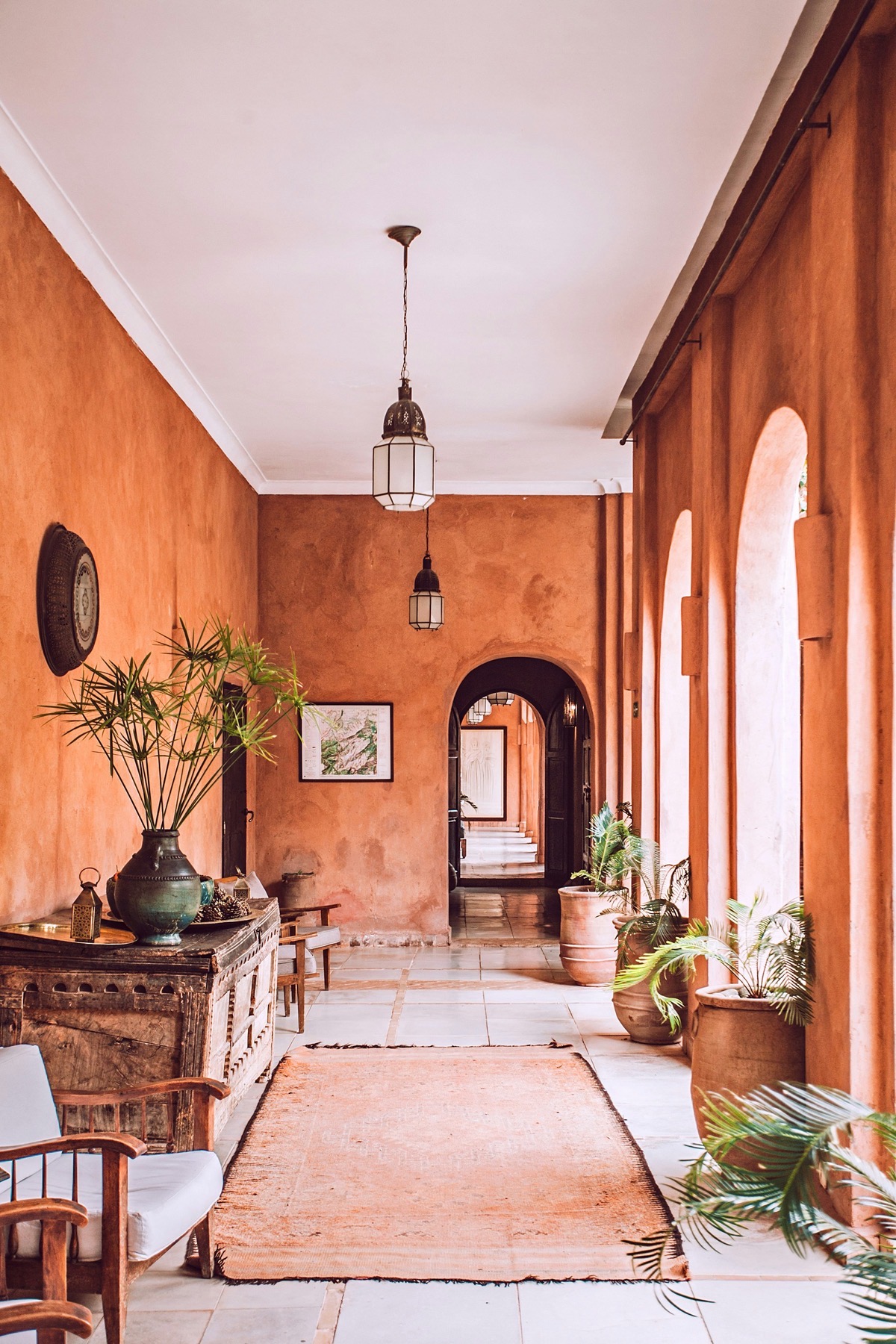 Terracotta-plastered riad corridor with glass lanterns and arched openings