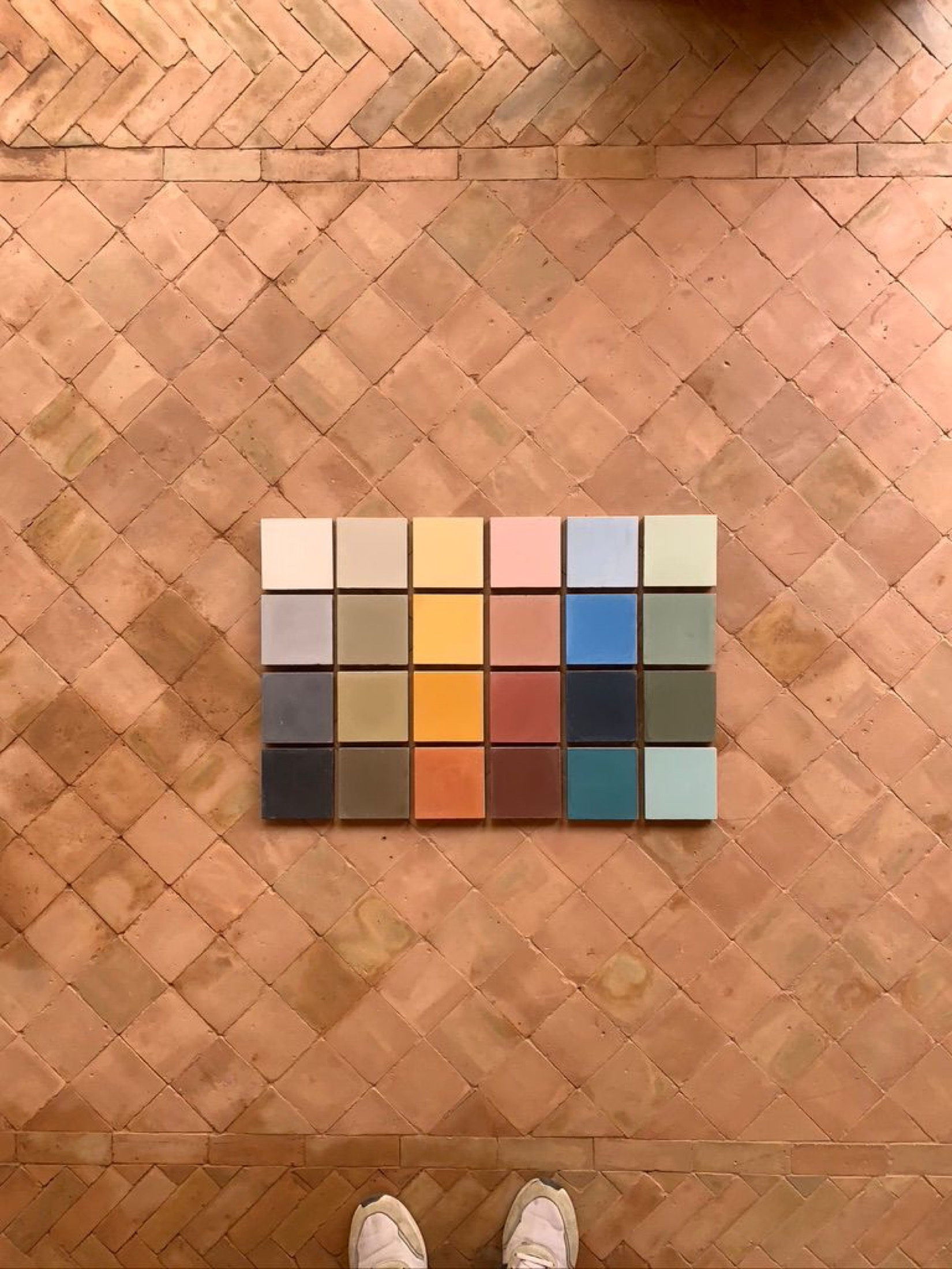 Zeljora's 24-color cement tile palette laid on a herringbone terracotta floor, photographed from above
