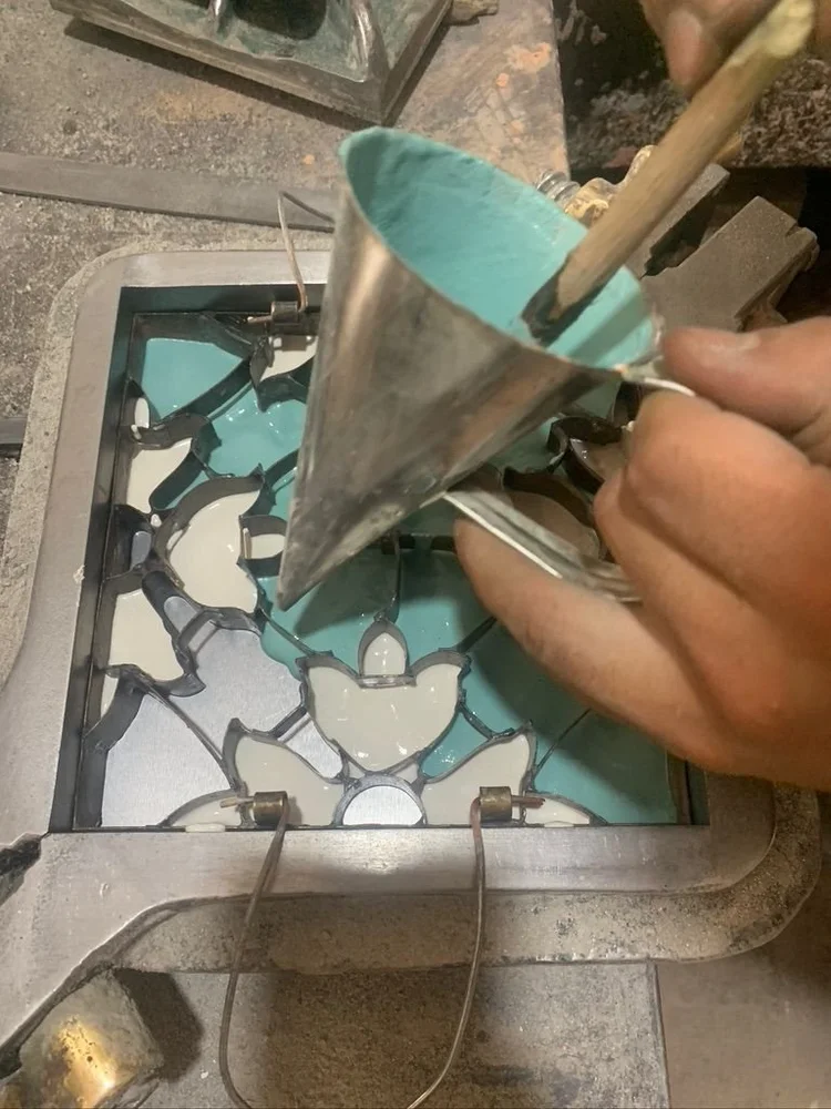 A conical funnel pouring teal pigmented cement slurry into a metal divider mold
